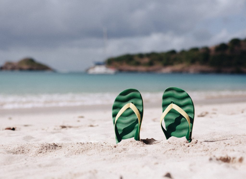 A pair of green flipflops sticking up in the sand on a sunny beach