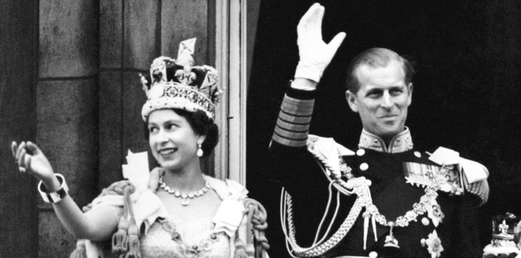 Black and white photo of a young Queen Elizabeth II and Prince Phillip, waving from their Buckingham Palace balcony