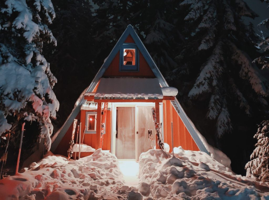 Photograph of a triangular hut, amongst fir trees, in the snow at night